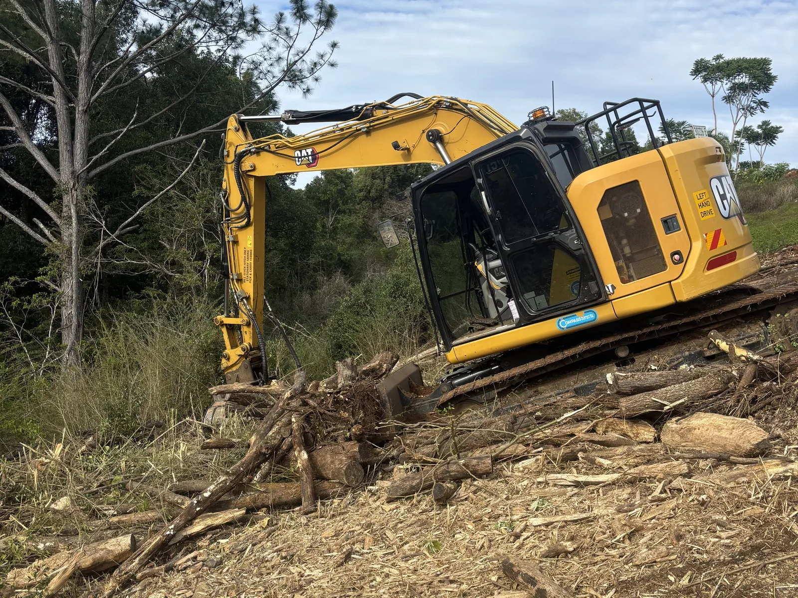 A yellow excavator clearing felled timber on a bush block