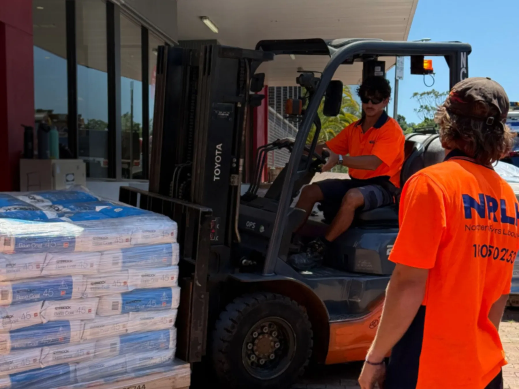 An NRLH labourer guiding a forklift loaded with pallets of bagged cement