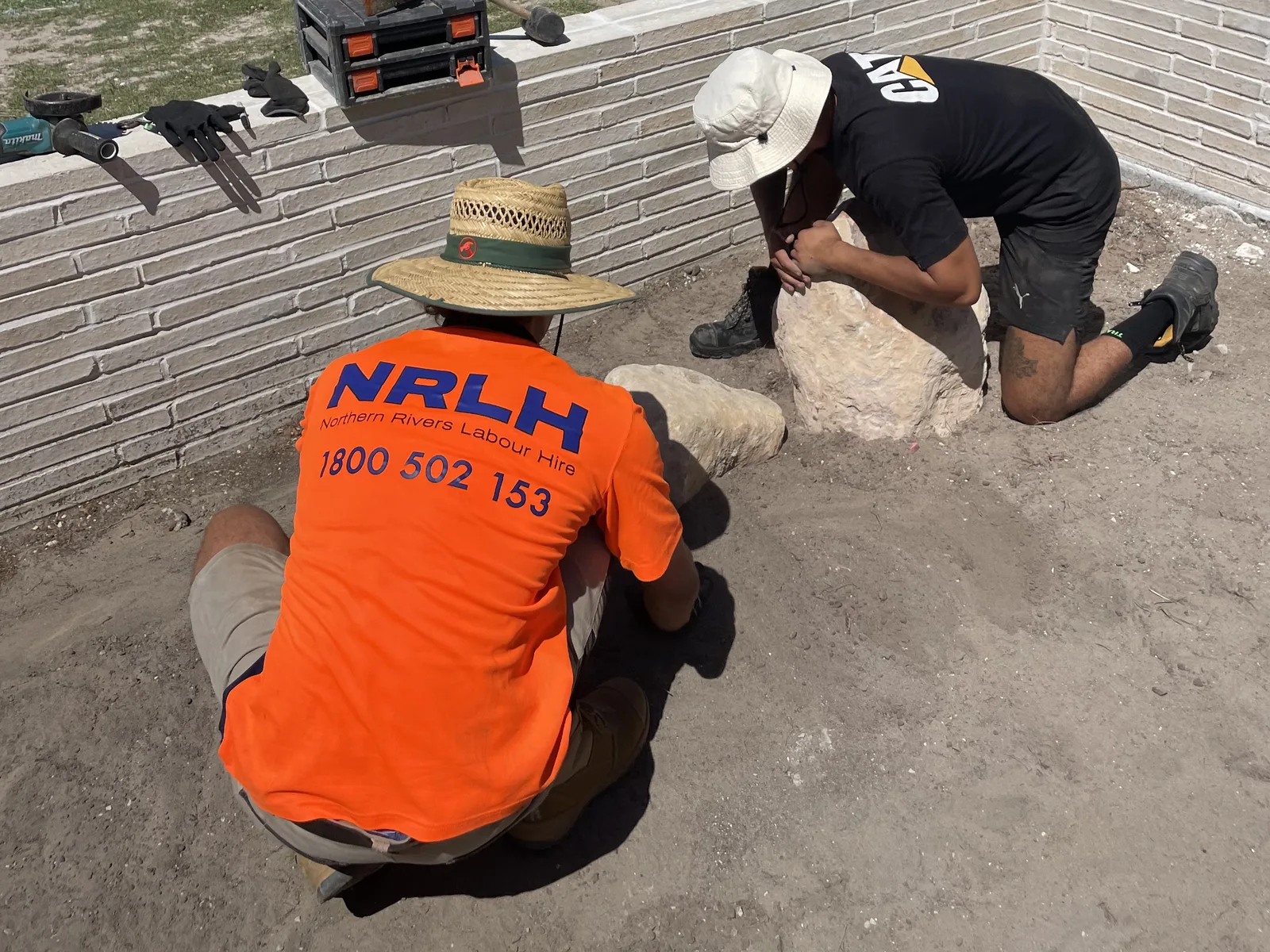 Two NRLH labourers bedding landscape rocks beside a new brick garden wall