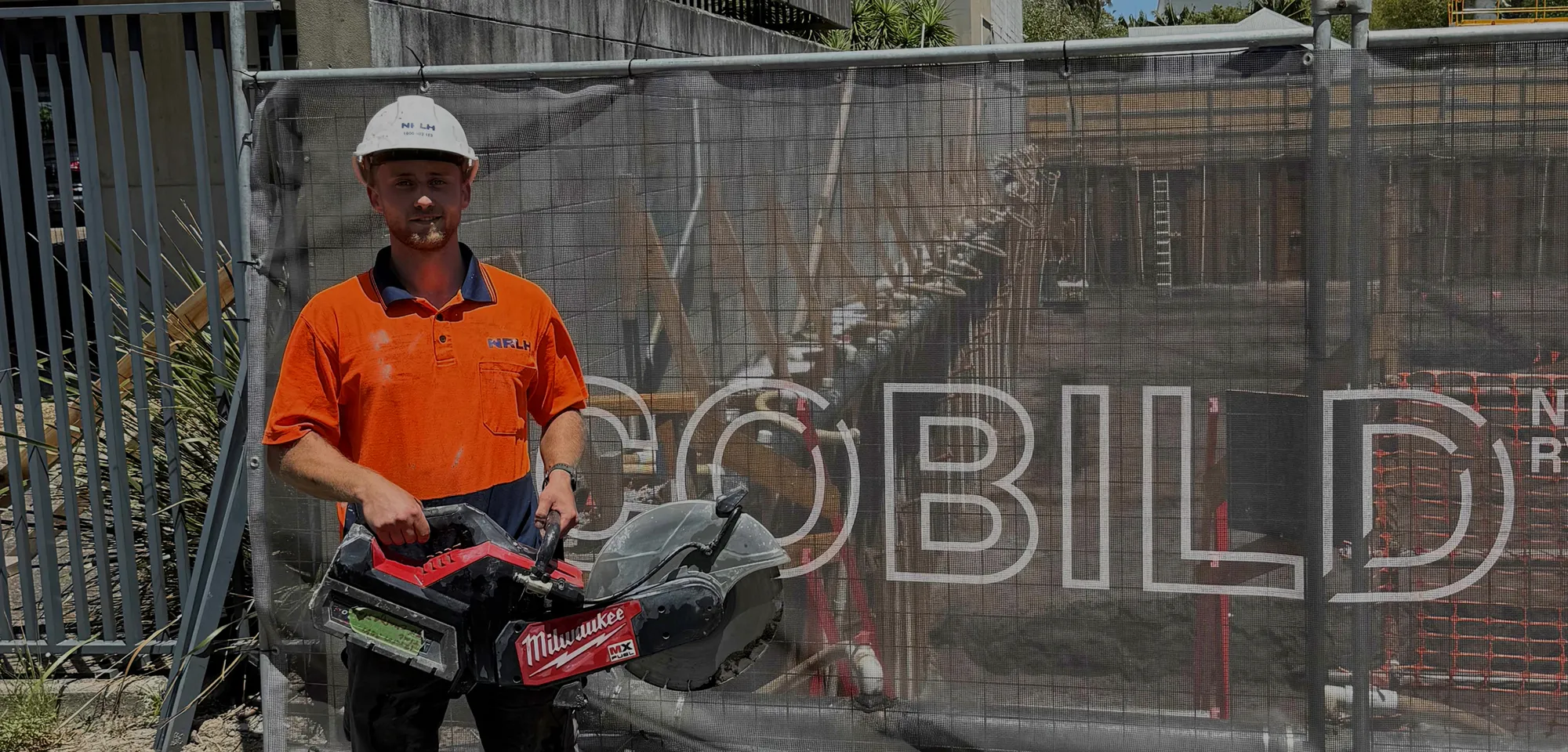An NRLH labourer in an NRLH hard hat holding a demolition saw beside site hoarding